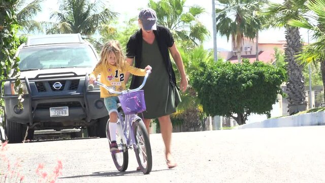 LOS CABOS MEXICO-2020: Woman Helping Girl With Yellow Shirt Ride Bike On Street In Front Of Nissan
