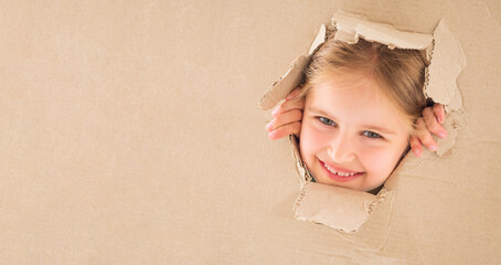 Funnt little girl looking through the torn hole in cardboard box