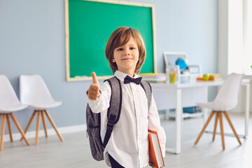 Back to school.Happy schoolboy with backpack smiling raised his thumb upstairs in class.