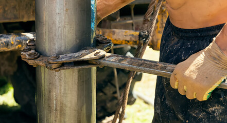 Worker driller holds drill pipes with a huge key