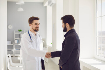 Handshake. Practicing doctor and patient shaking hands smiling at the clinic.