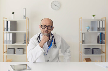 Senior doctor conducting online consultation from his medical office. Mature medic listening to...