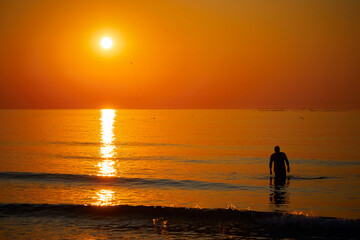 Naklejka na ściany i meble Silhouette of a man swimming in the sea at sunrise