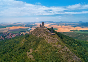 Fototapeta premium Aerial view of two stone towers, ruins of medieval castle Hazmburk, Hasenburg built on top of the mountain peak, surrounded by agriculture czech landscape. Tourist point, castles of western Bohemia