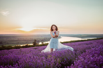 Fototapeta na wymiar A beautiful young girl against the sunset and a beautiful sky in a lavender field. Purple lavender, orange sky, empty space for text. Advertising photo of perfume, makeup, fashion, lavender, beauty.