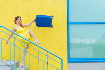 A happy red-haired woman in a yellow dress is walking down the stairs and joyfully swing a blue...