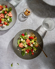 Salad of strawberries, herbs, cucumber and cheese on gray plates with sharp shadows