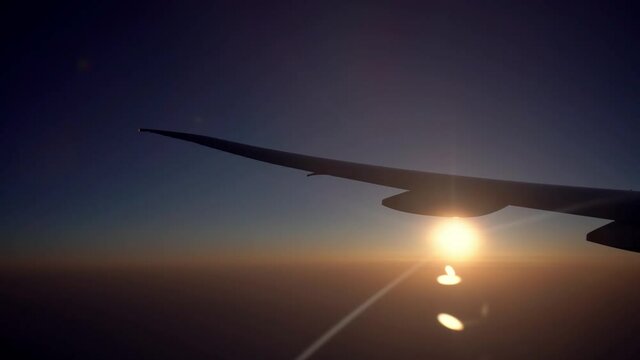 4K, View of plane wing with the sunset through an airplane window in flight trip, traveling by air. Plane flying with beautiful dawn sun. Vacation journey concept-Dan