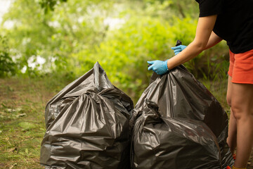 People collect garbage in bags. Hands tie a bag. Collect garbage in nature. The concept of cleaning in nature. Clean the green area. Collect garbage in gloves. Black bags. trash 