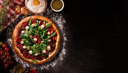 Brazilian pizza with dried tomato, arugula and mustard. Top view on black concrete background, close up. Traditional Brazilian Pizza