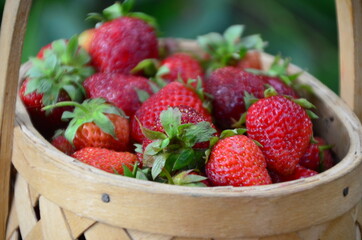 Ripe strawberries with leaves in wicker basket on wooden table on blurred background