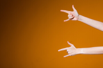 Female hands show rock sign with fingers on an orange background. Concept of isolated signs and gestures.
