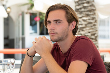 a focused handsome young man looking at the distance while sitting at an outdoor bar terrace
