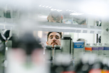 reflection in the mirror of a man choosing medication at a pharmacy