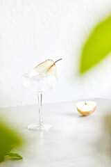 Classic martini with ice. Female hand decorates cocktail with pear slice. On a light background