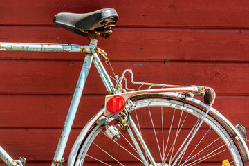 An old, blue and rusty bicycle leaning against a red, wooden wall