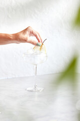 Classic martini with ice. Female hand decorates cocktail with pear slice. On a light background