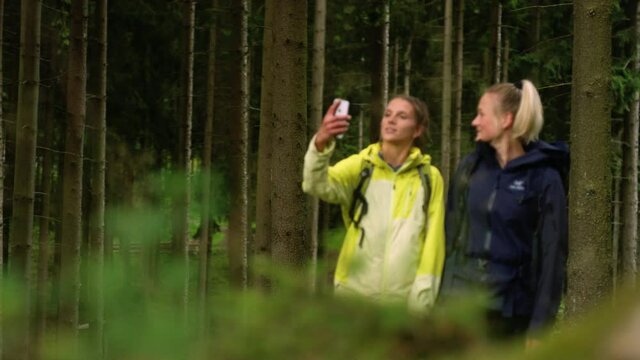 Two Women Taking a Selfie on a Hike through the Woods. Taking a Picture in Nature for social media. Walking through a Forest in the Rain.