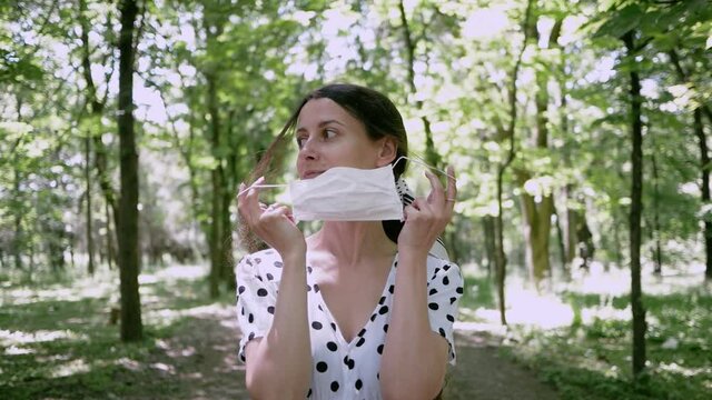 Young woman removes mask while nobody sees and puts on, she makes breath of fresh air in Park. concept of removing limitations of pandemic or end of Allergy