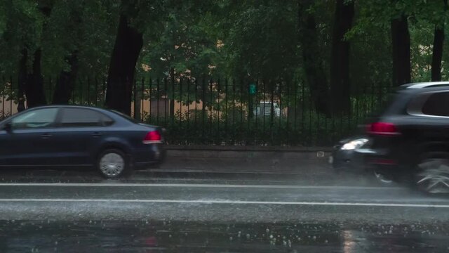 Downpour on the City Streets. The car moves past the camera and rides through the puddle. From under the wheel rises a beautiful stream of water