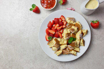 Kaiserschmarren or Kaiserschmarrn, traditional Austrian or German sweet pancake dessert, with berry, strawberry jam or rote grutze and vanilla pudding sauce. Top view. Copy space.