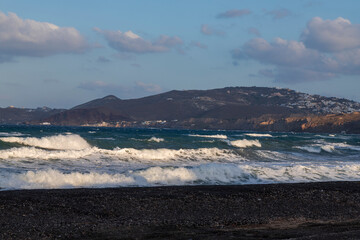 Beautiful black beach with coast and sea in Vlichada with blue sky background with white clouds and sea.