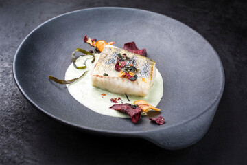 Traditional fried skrei cod fish with vegetable chips and algae in a lemon coconut sauce offered as close-up in a modern design plate with copy space