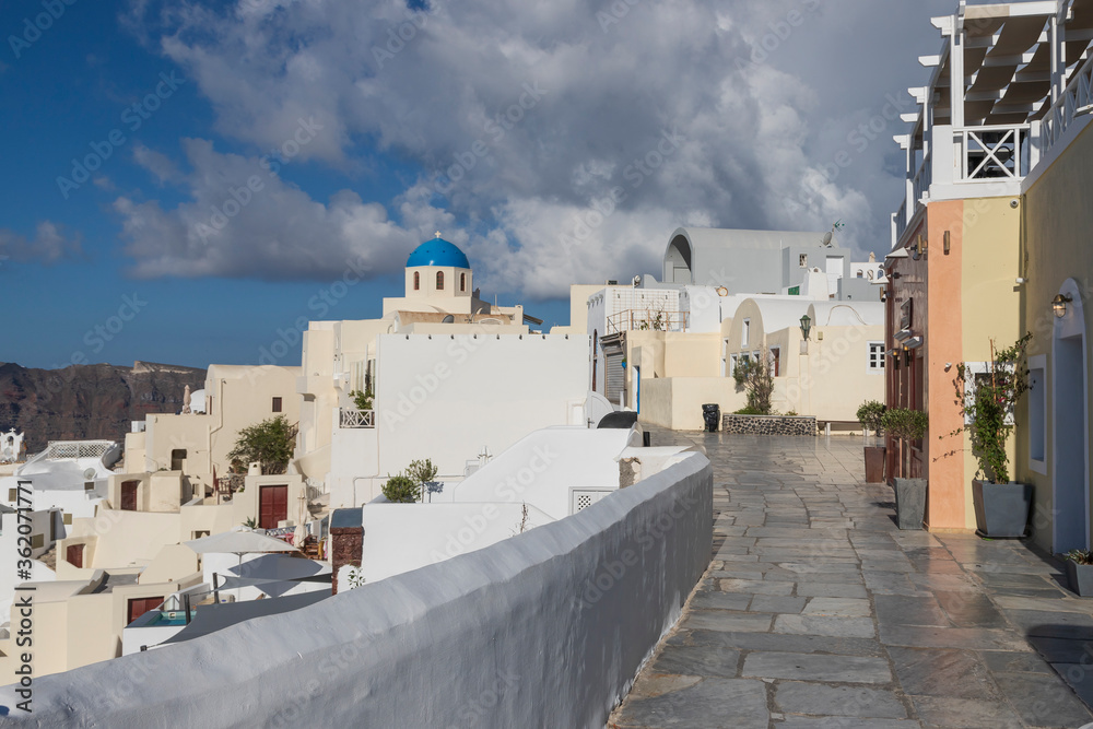 Wall mural Oia town on Santorini island in Greece. The background is a blue sky with dark clouds. View of white houses