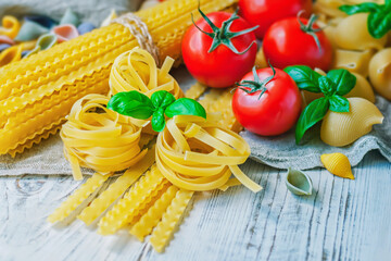 Various types of Italian pasta, tomatoes and Basil leaves on a wooden background, selective focus.