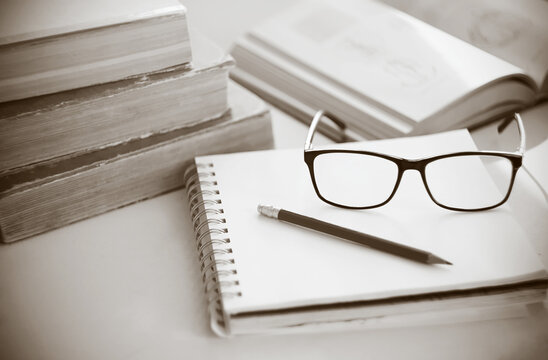 A single-color image of the workplace, where old books, notepad, pencil, and glasses lie.