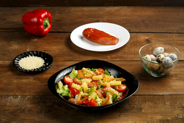 Pan-Asian salad with in a black plate and a row of ingredients on a wooden table.