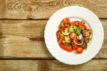 On a wooden table is a white plate of boiled mung bean with vegetables and mushrooms. Copy space.