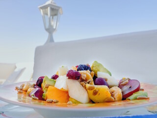 a large plate with pieces of fresh fruit chopped, on an implied outdoor table in front of a white...