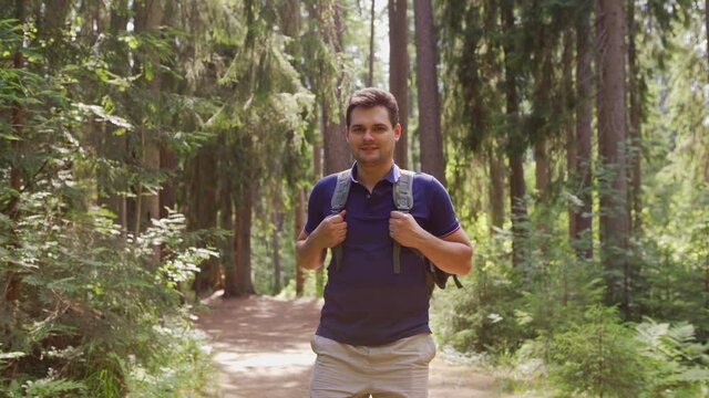 Tilt dowm medium shot of smiling middle aged hiker with backpack walking on trail in forest, stopping and looking at camera feeling happy