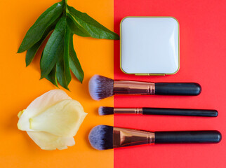 Obraz na płótnie Canvas premium makeup brushes and blush on a colored red and orange background, creative cosmetics flat lay, copy space