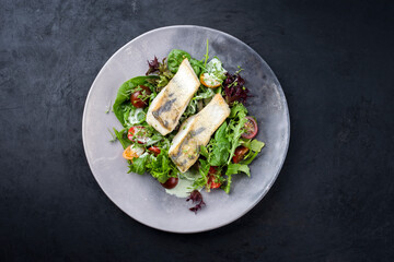 Traditionelles gebratenes Skrei Fisch Filet mit italienischen Salat und Tomaten in Zitonen Kokos Sauce  angeboten als Draufsicht in einem Modern Design Teller mit Textfreiraum 