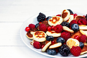 Trendy mini pancakes breakfast concept. Tiny  cereal Pancakes with berries, honey or maple syrup on white background. Kids lovely breakfast concept