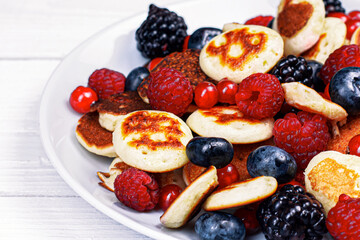 Trendy mini pancakes breakfast concept. Tiny  cereal Pancakes with berries, honey or maple syrup on white background. Kids lovely breakfast concept