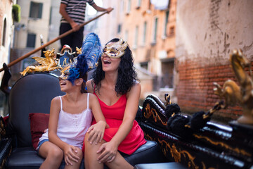 A mother is having fun with her daughter on gondola at Venice, Italy. Venetian mask and family concept. - obrazy, fototapety, plakaty