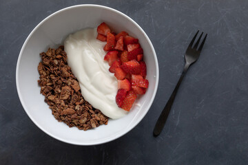 Bowl with granola, Greek yogurt and strawberries on a dark grey background