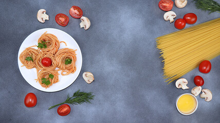 Obraz na płótnie Canvas Italian pasta spaghetti and ingredients for cooking, cherry tomatoes, olive oil and spices on a dark table, top view, place for text