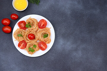 Italian pasta spaghetti with cherry tomatoes, olive oil and spices on a dark table, top view, place for text