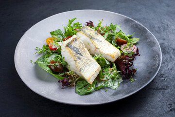 Traditiomelles gebratenes Skrei Kabeljau Fisch Filet mit italienischen Salat und Tomaten in Zitronen Kokos Dressing angeboten als close-up in einem Modern Design Teller