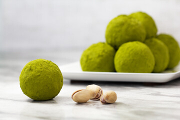 Homemade energy balls with dried apricots, raisins, dates, prunes, walnuts, pistachios and green matcha. Healthy sweet food. Energy balls in a plate on a marble grey background. Close up. Side view.