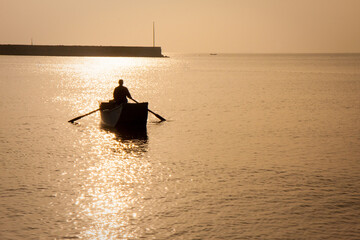 silhouette of man rowing fishing boat in water during dusk and golden hour in Lima Peru