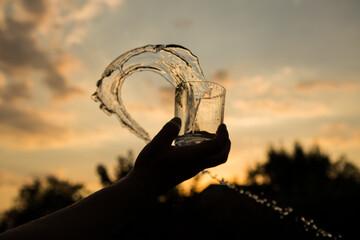 Splash of water in a glass. Flying water. A glass of water in a man's hand in the sunset.