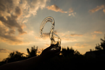 Splash of water in a glass. Flying water. A glass of water in a man's hand in the sunset.