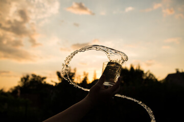 Splash of water in a glass. Flying water. A glass of water in a man's hand in the sunset.