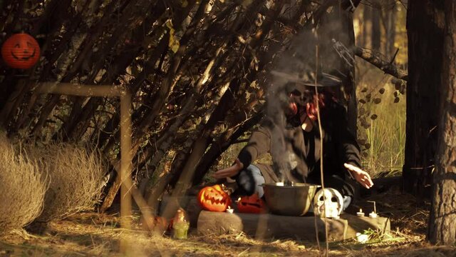 Witch prepares a potion in a cauldron in a forest hut. Theme of the occult and esoteric rituals in the wild nature. Mystical wizard uses a cauldron to perform a mystical ceremony.