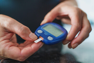 Medicine, Diabetes, Glycemia, Health care and people concept - close up of female using lancelet on finger to checking blood sugar level by Glucose meter